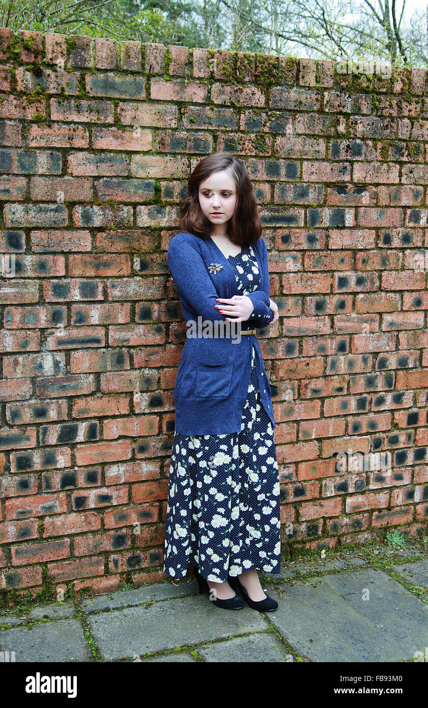 Giovane donna in piedi accanto a un muro di mattoni guardando preoccupato vestito in un 1940s style Foto Stock