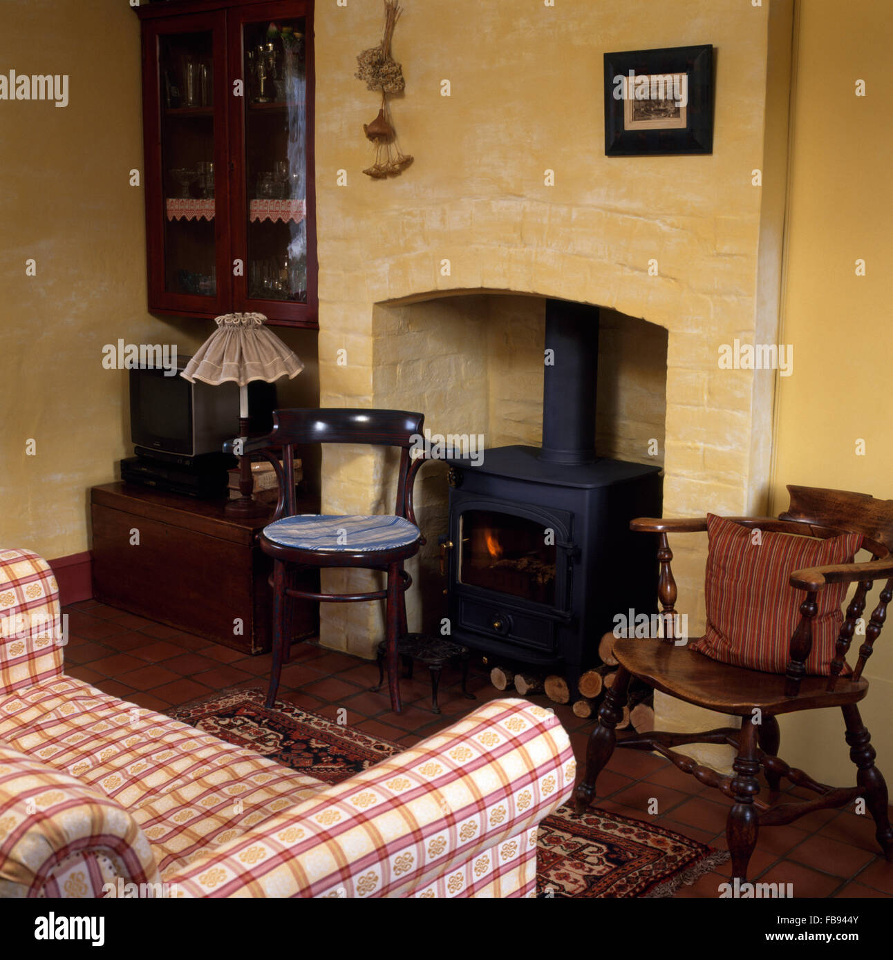 Sedie in legno su entrambi i lati del camino con stufa a legna in cottage in salotto con un rosso controllato divano Foto Stock