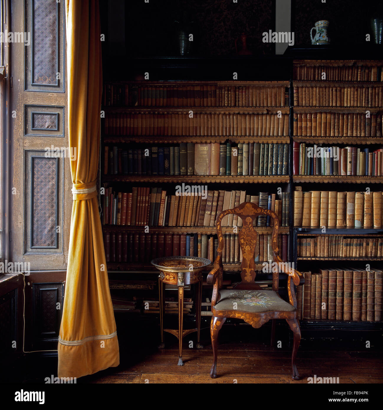 Antiquariato sedia intarsiato e un piccolo tavolo di fronte a scaffali con pelle antichi libri rilegati in country house library Foto Stock