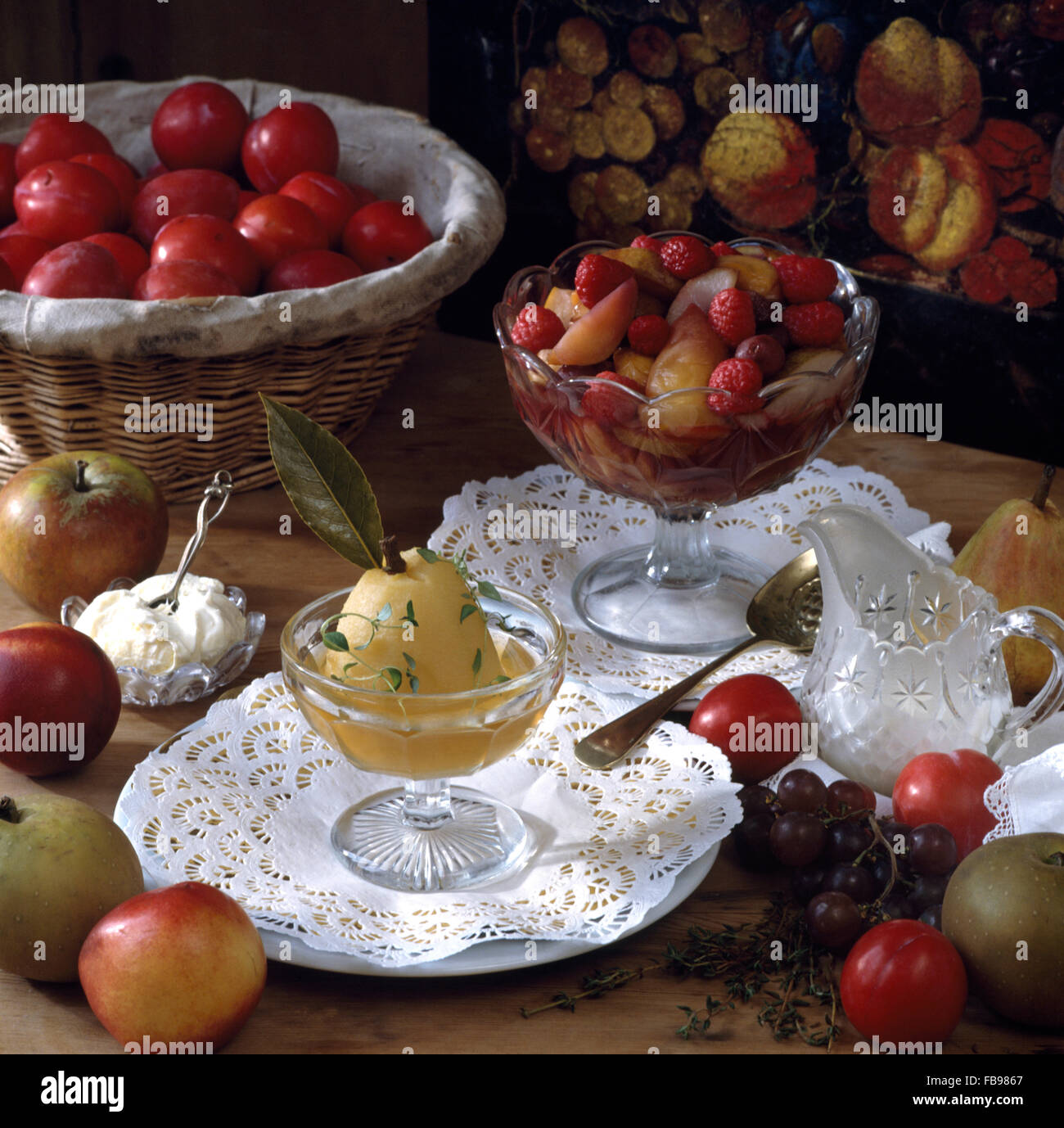 Pera affogata e misto frutta affogato in piatti in vetro sulla tavola con un cesto di prugne fresche Foto Stock