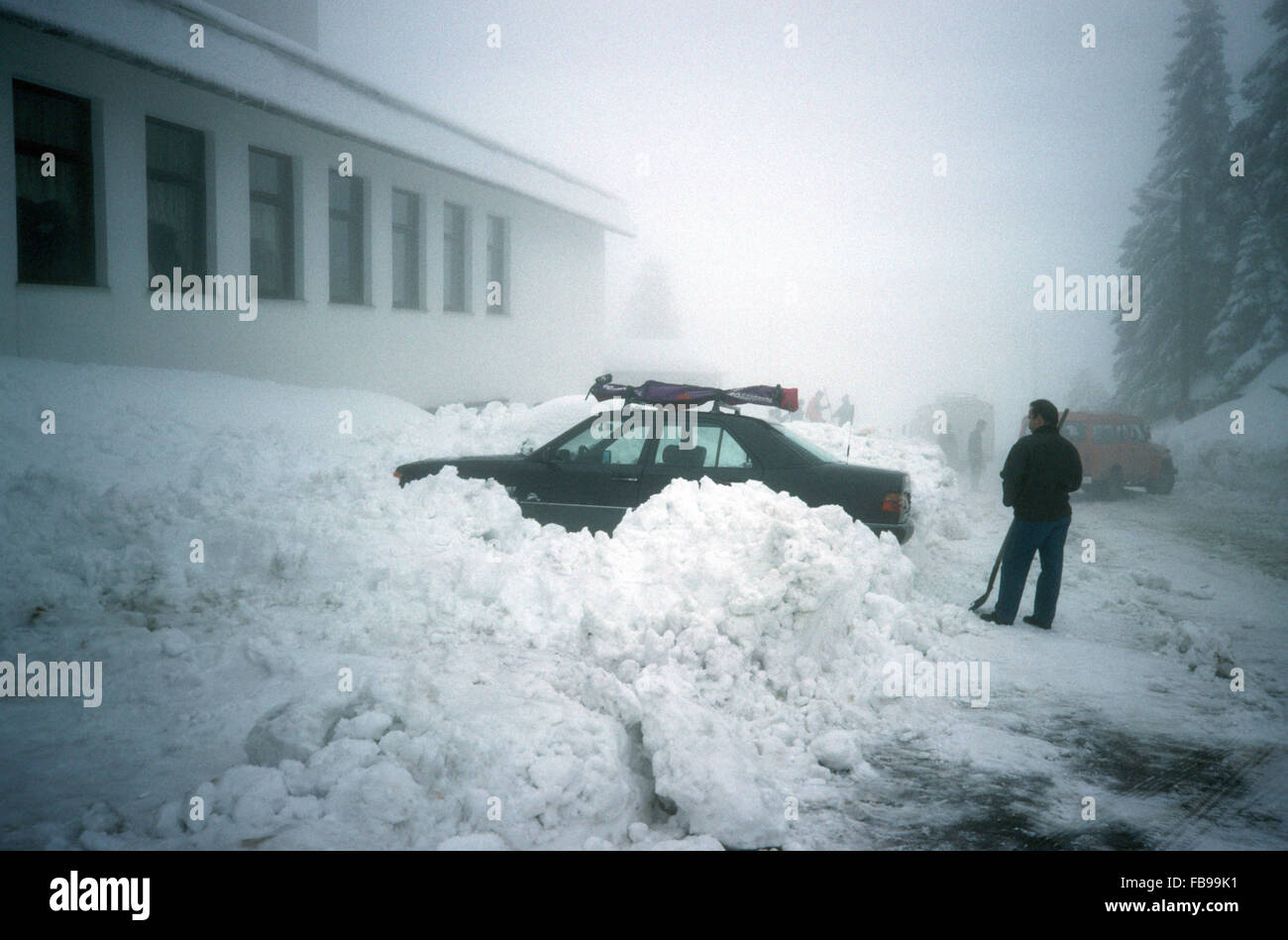 Uomo in piedi da una macchina bloccata in un snow drift Foto Stock