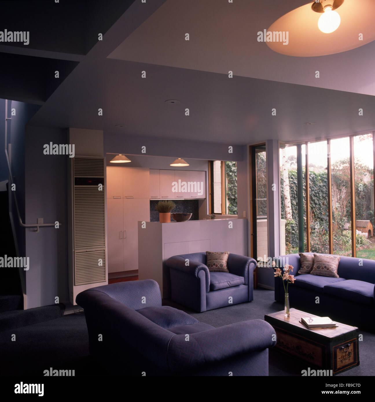 Blu pallido divani e poltrone in un piano aperto degli anni novanta spazio soggiorno con una vista della cucina Foto Stock