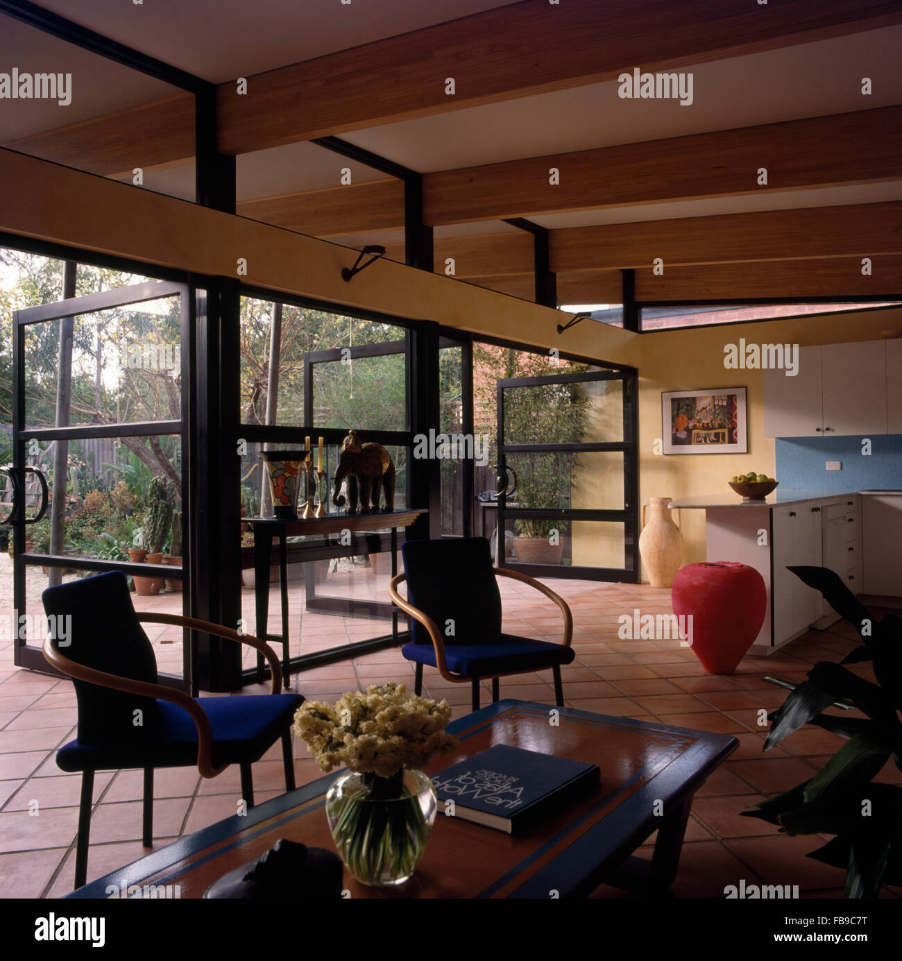 Sedie blu e un alto edificio rosso pot in un salotto a pianta aperta con porte in vetro Foto Stock