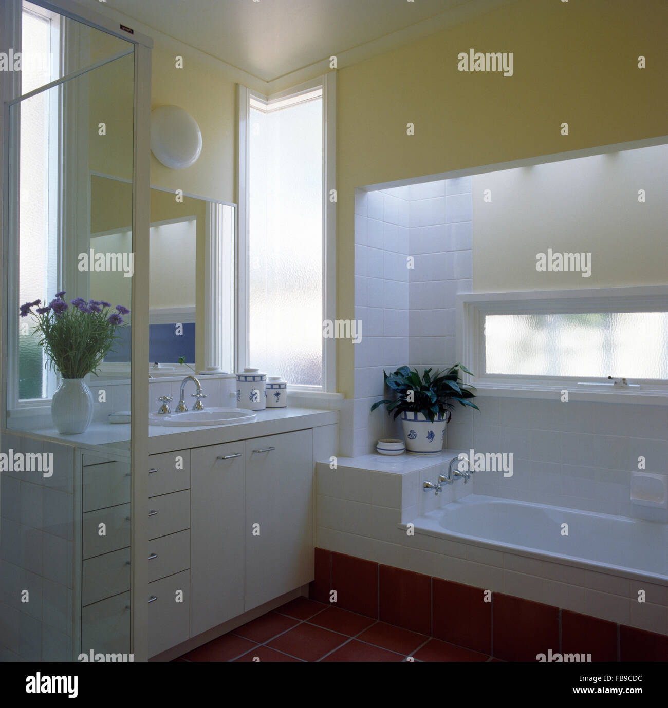 Bianco unità vanity e piastrelle in un giallo pallido degli anni novanta bagno con una finestra stretta al di sopra di un basso bagno attrezzato Foto Stock