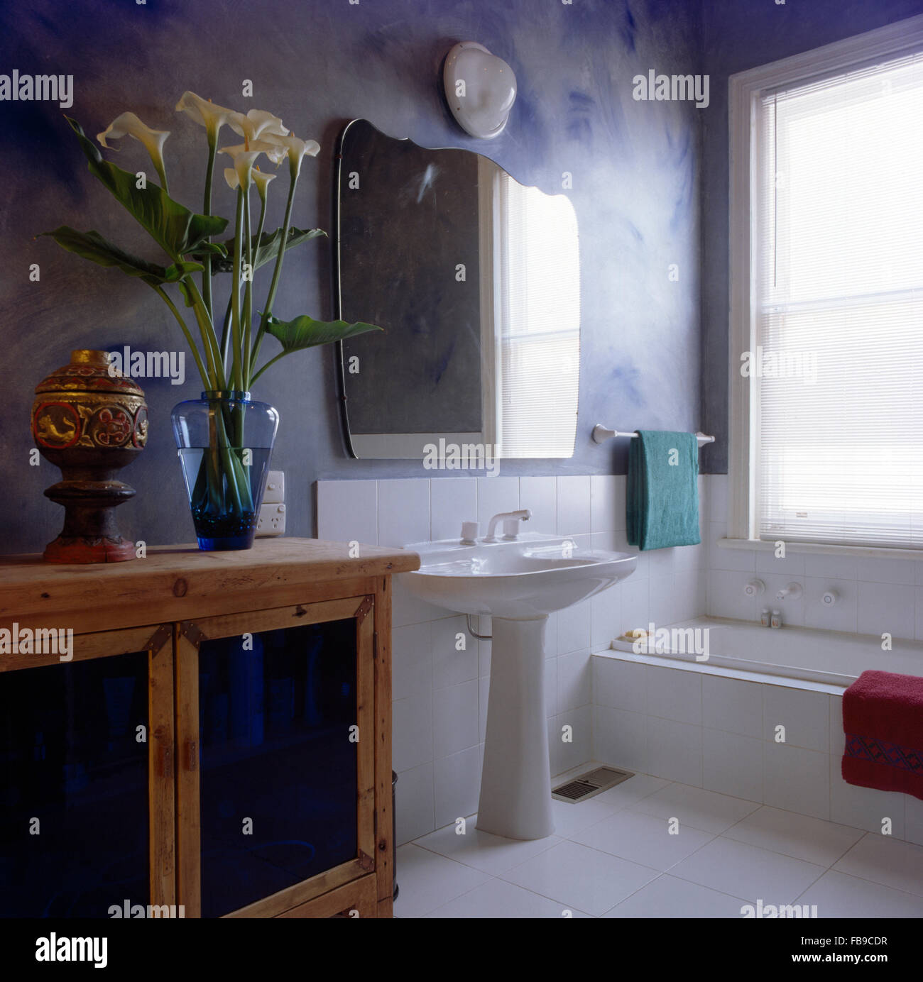 Specchio sopra lavello in blu e bianco bagno con un vaso di bianco arum gigli sulla credenza Foto Stock