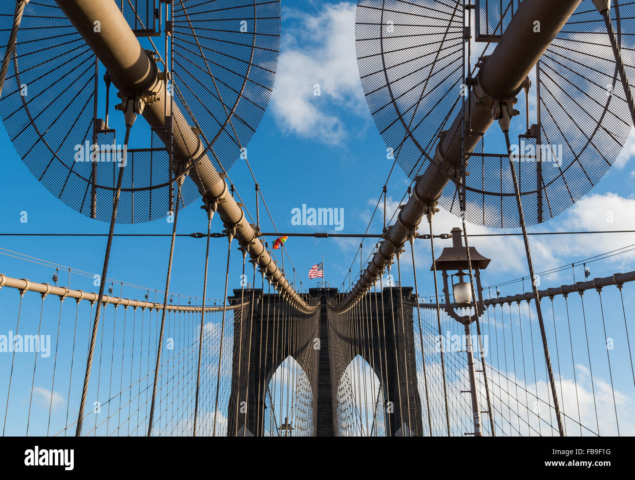 Guardando lungo il ponte di Brooklyn verso una delle torri con cavi di sospensione e una bandiera americana battenti. NYC. Foto Stock