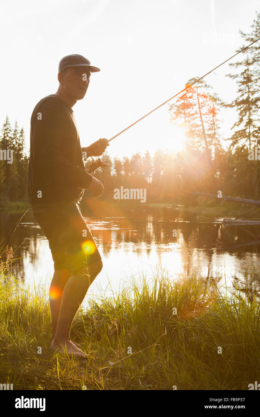 La Svezia, Vastmanland, Svartalven, l uomo con la canna da pesca in presenza di luce solare Foto Stock