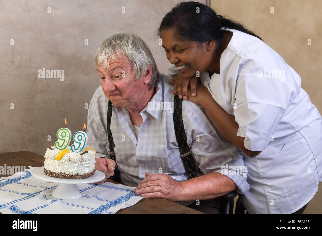 Uomo anziano in casa di cura soffiando le candeline sulla sua torta di compleanno Foto Stock