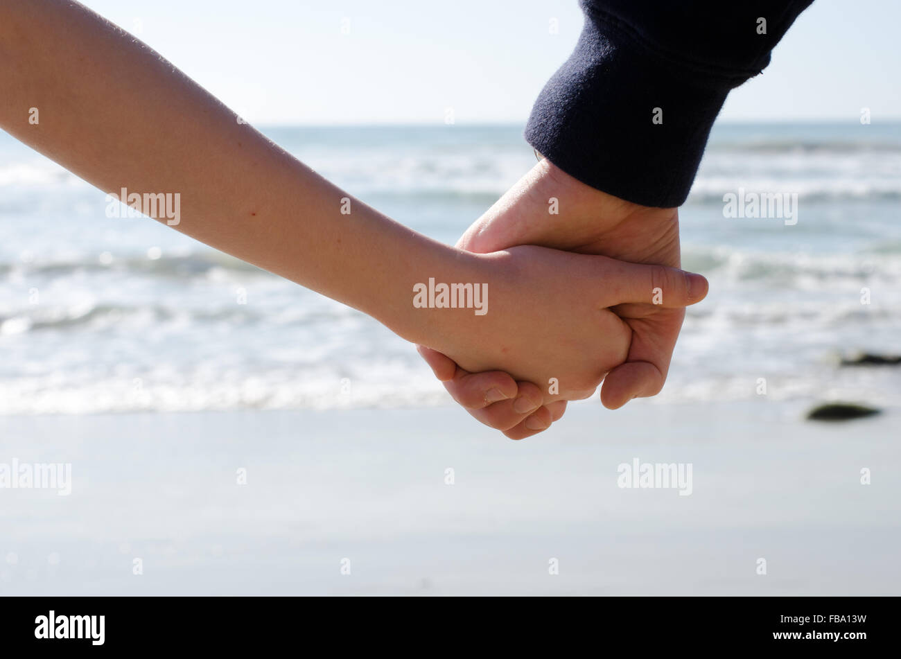 Un ragazzo e una ragazza tenendo le mani con il mare in background Foto Stock