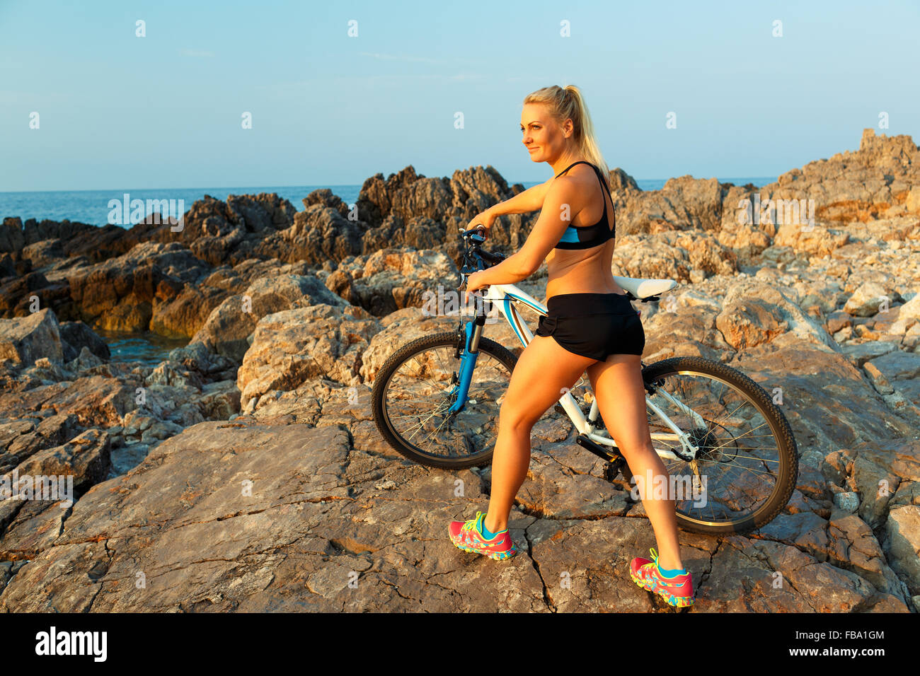 Felice athletic giovane donna in piedi sulle rocce con una bicicletta e godetevi la vista Foto Stock