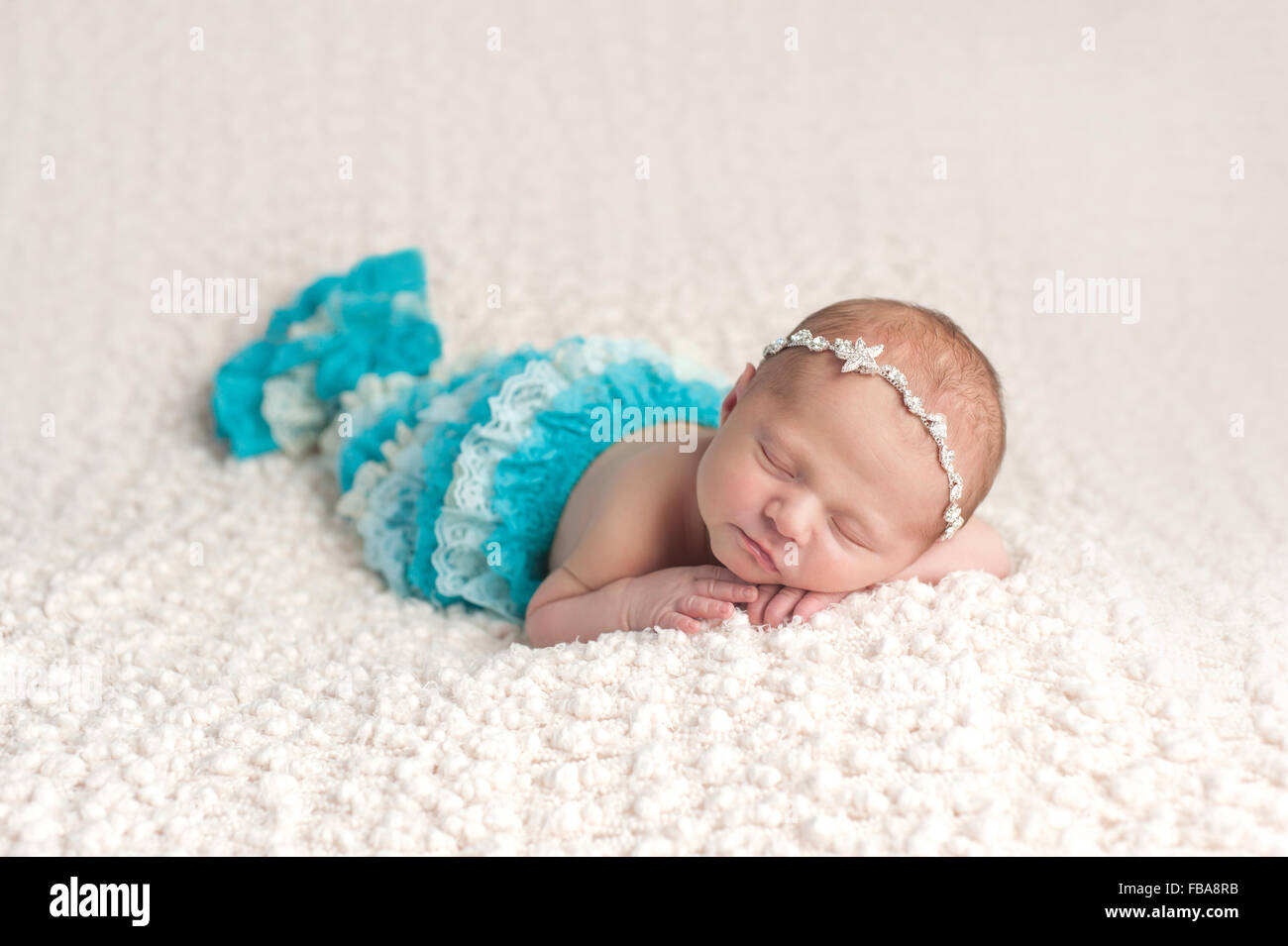 Un sonno, dieci giorni di età neonato bambina indossa un laccio aqua blue mermaid coda. Ella è sdraiato sul suo stomaco su una crema colorata, Foto Stock