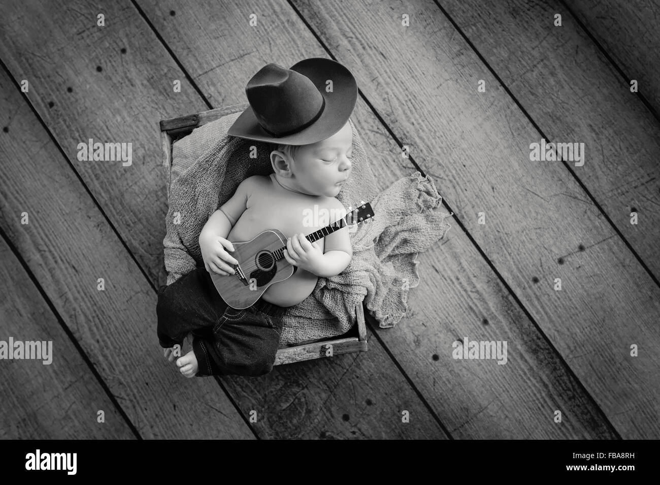 Un b&w immagine di un tre settimane vecchio baby boy indossando un cappello da cowboy e jeans e la riproduzione di una piccola chitarra acustica. Egli è giacente in un woo Foto Stock