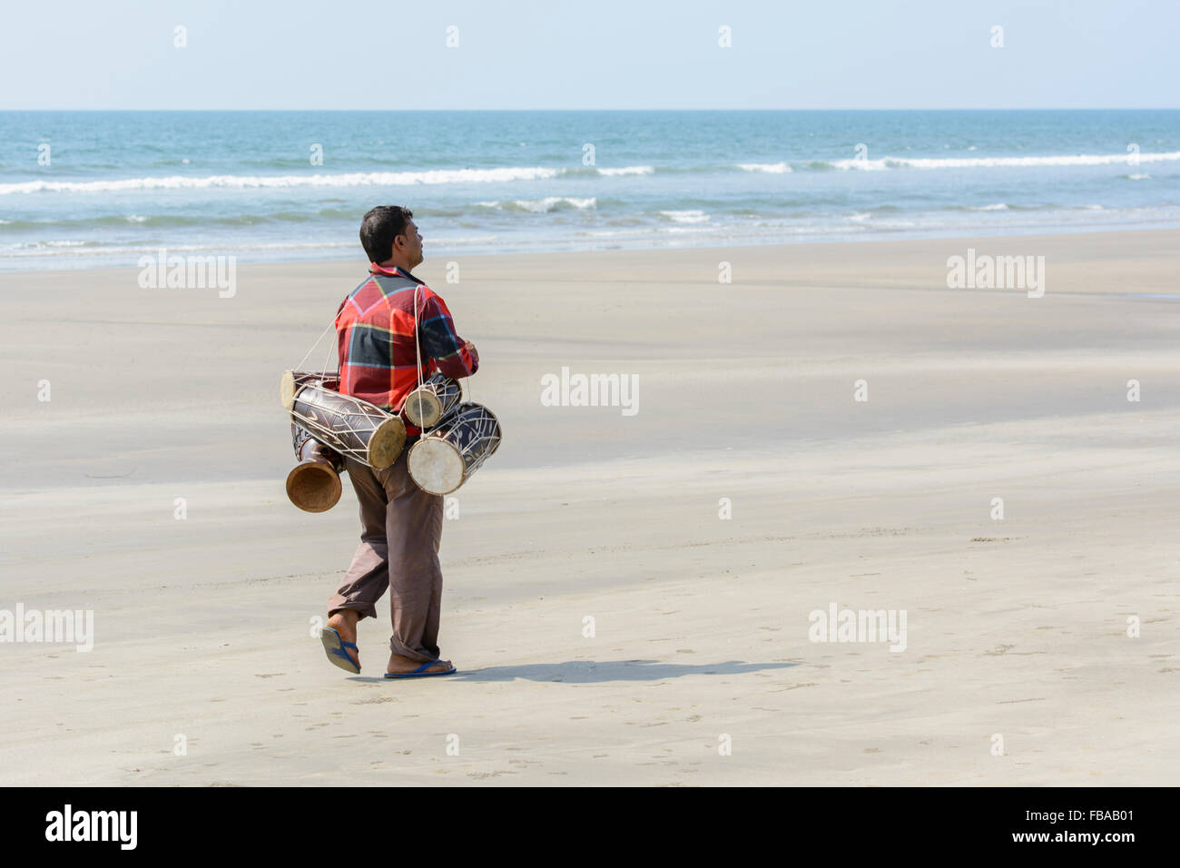 Un indiano di vendita man mano tradizionali tamburi passeggiate lungo una spiaggia deserta, Mandrem beach, a Nord Goa, India Foto Stock