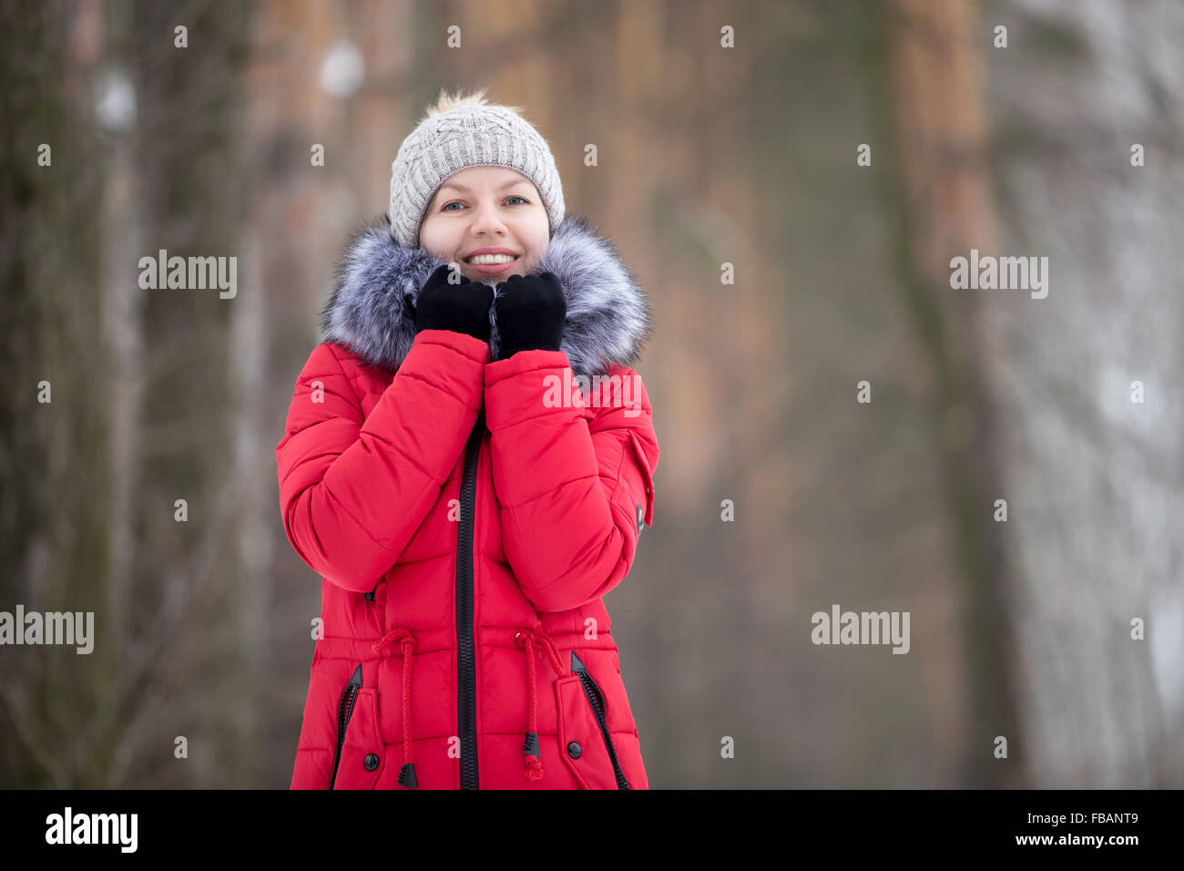 Sorridente ragazza bella in berretto lavorato a maglia e rosso cappotto invernale stessa di incarto fino in pelliccia collare, all'aperto, guarda nella telecamera Foto Stock