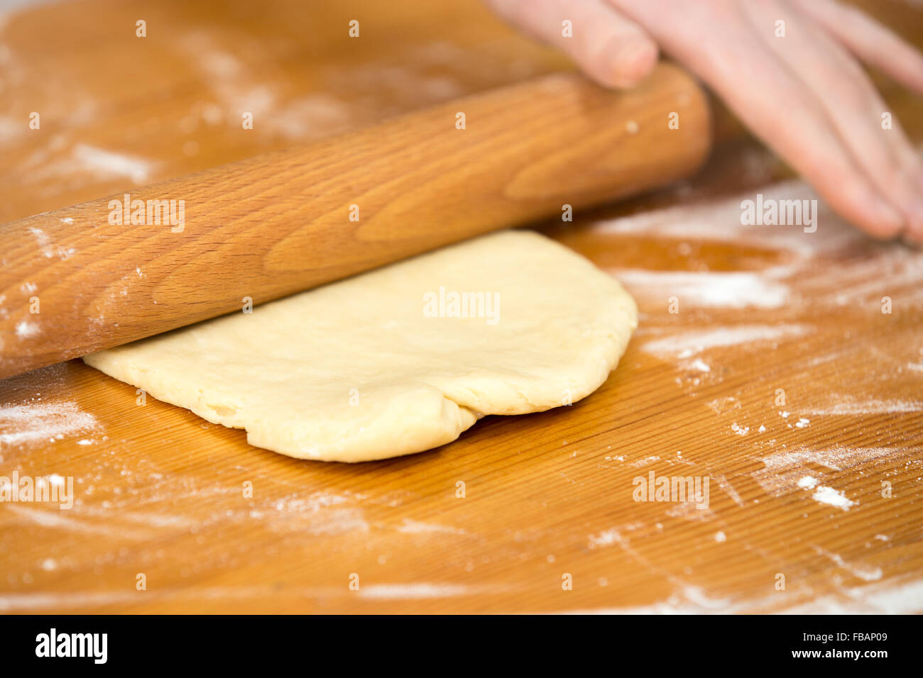 Chiudere la cucina casalinga, mani femminili stendete la pasta con pasta di legno rullo sul tavolo di legno ricoperti di farina Foto Stock