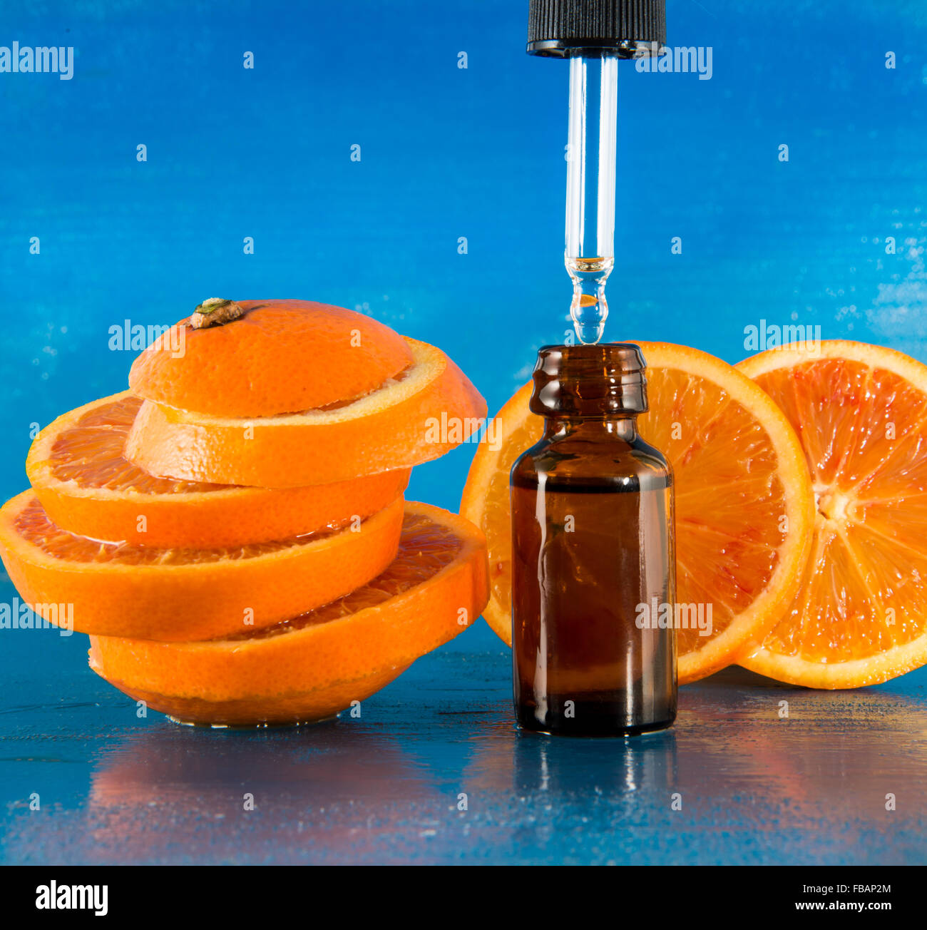 Olio Essenziale di Arancio Ambra Flacone con contagocce e fresche fettine di arancia, con sfondo blu Foto Stock