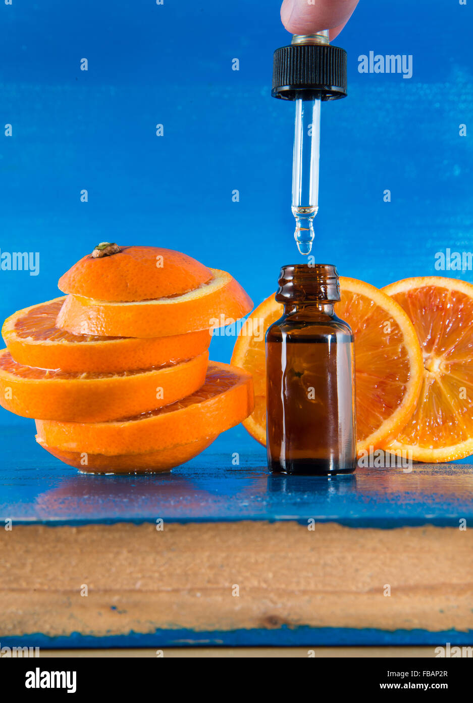 Olio Essenziale di Arancio Ambra Flacone con contagocce e fresche fettine di arancia, con sfondo blu Foto Stock