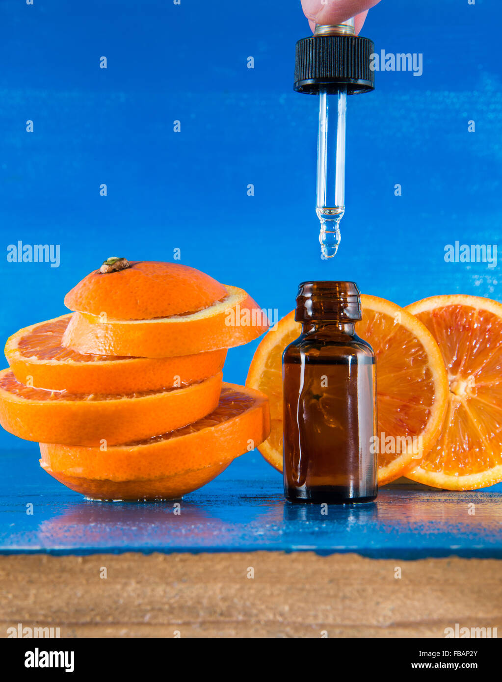 Olio Essenziale di Arancio Ambra Flacone con contagocce e fresche fettine di arancia, con sfondo blu Foto Stock
