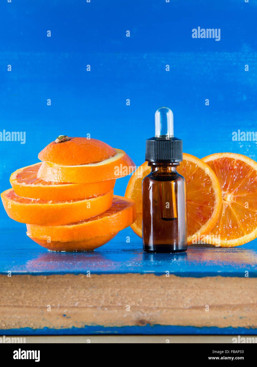 Olio Essenziale di Arancio Ambra Flacone con contagocce e fresche fettine di arancia, con sfondo blu Foto Stock