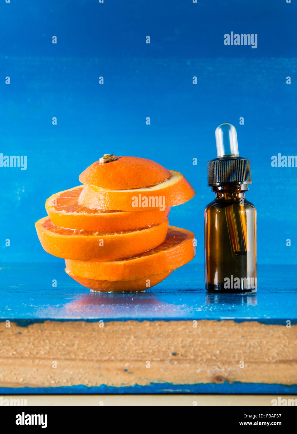 Olio Essenziale di Arancio Ambra Flacone con contagocce e fresche fettine di arancia, con sfondo blu Foto Stock