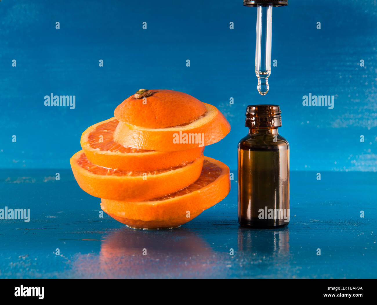 Olio Essenziale di Arancio Ambra Flacone con contagocce e fresche fettine di arancia, con sfondo blu Foto Stock