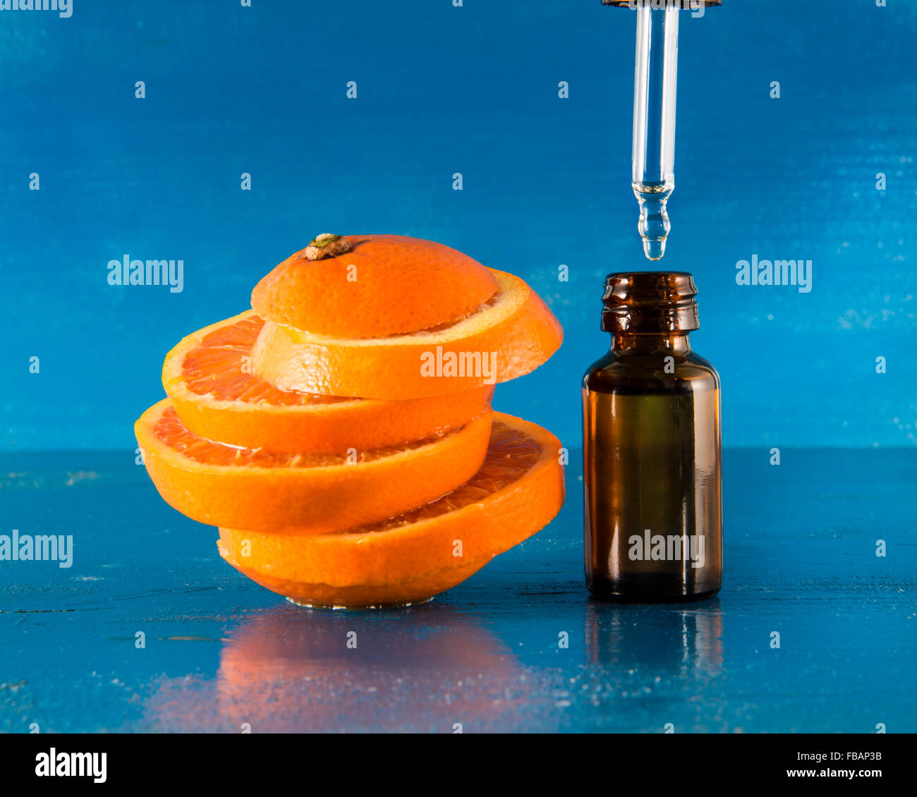 Olio Essenziale di Arancio Ambra Flacone con contagocce e fresche fettine di arancia, con sfondo blu Foto Stock
