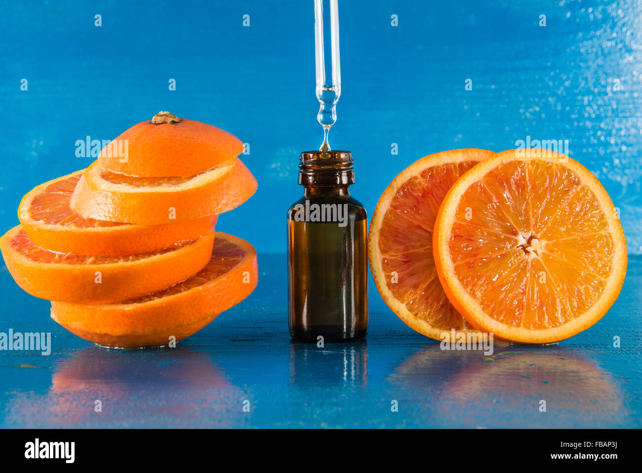 Olio Essenziale di Arancio Ambra Flacone con contagocce e fresche fettine di arancia, con sfondo blu Foto Stock