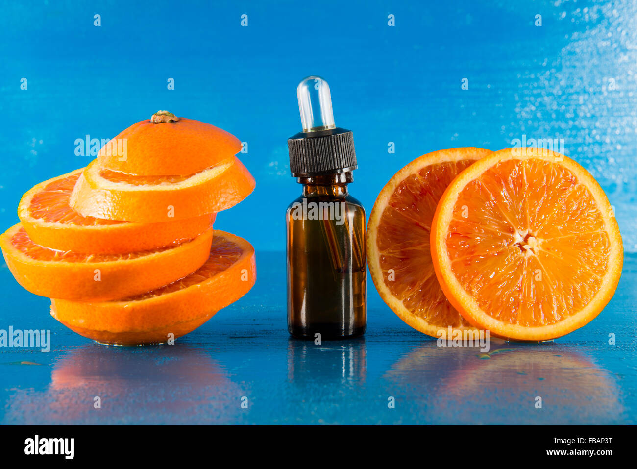 Olio Essenziale di Arancio Ambra Flacone con contagocce e fresche fettine di arancia, con sfondo blu Foto Stock
