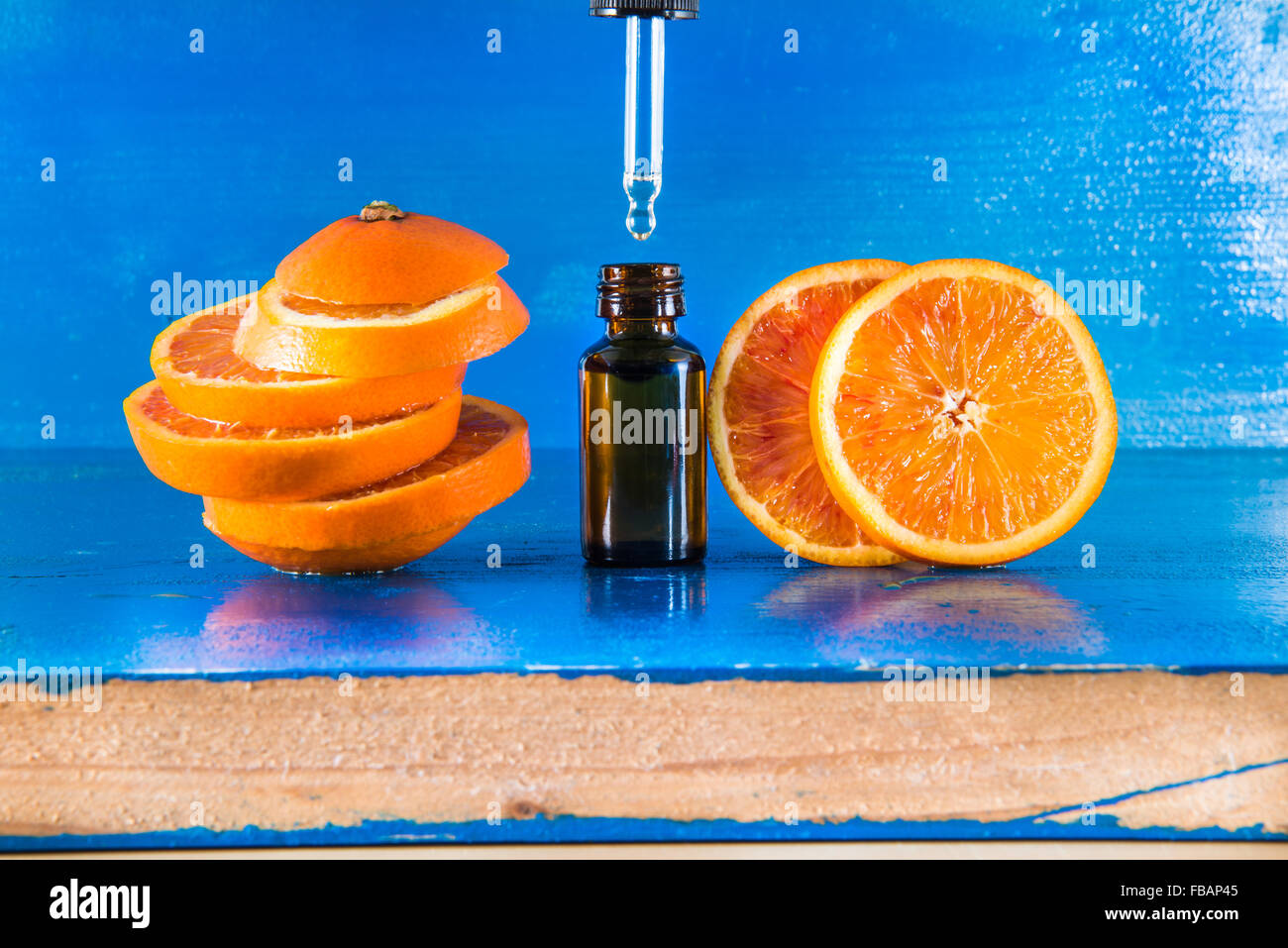 Olio Essenziale di Arancio Ambra Flacone con contagocce e fresche fettine di arancia, con sfondo blu Foto Stock