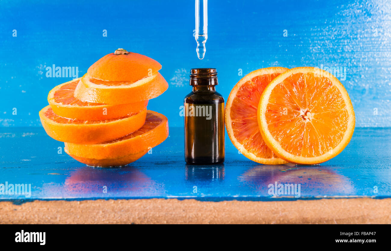 Olio Essenziale di Arancio Ambra Flacone con contagocce e fresche fettine di arancia, con sfondo blu Foto Stock