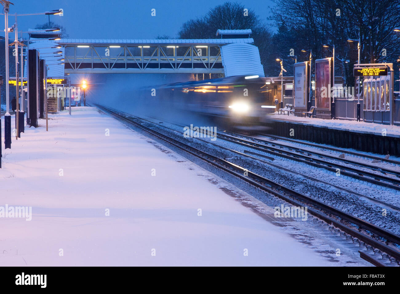 Un treno passa attraverso West Byfleet stazione su una nevoso inverno del giorno Foto Stock