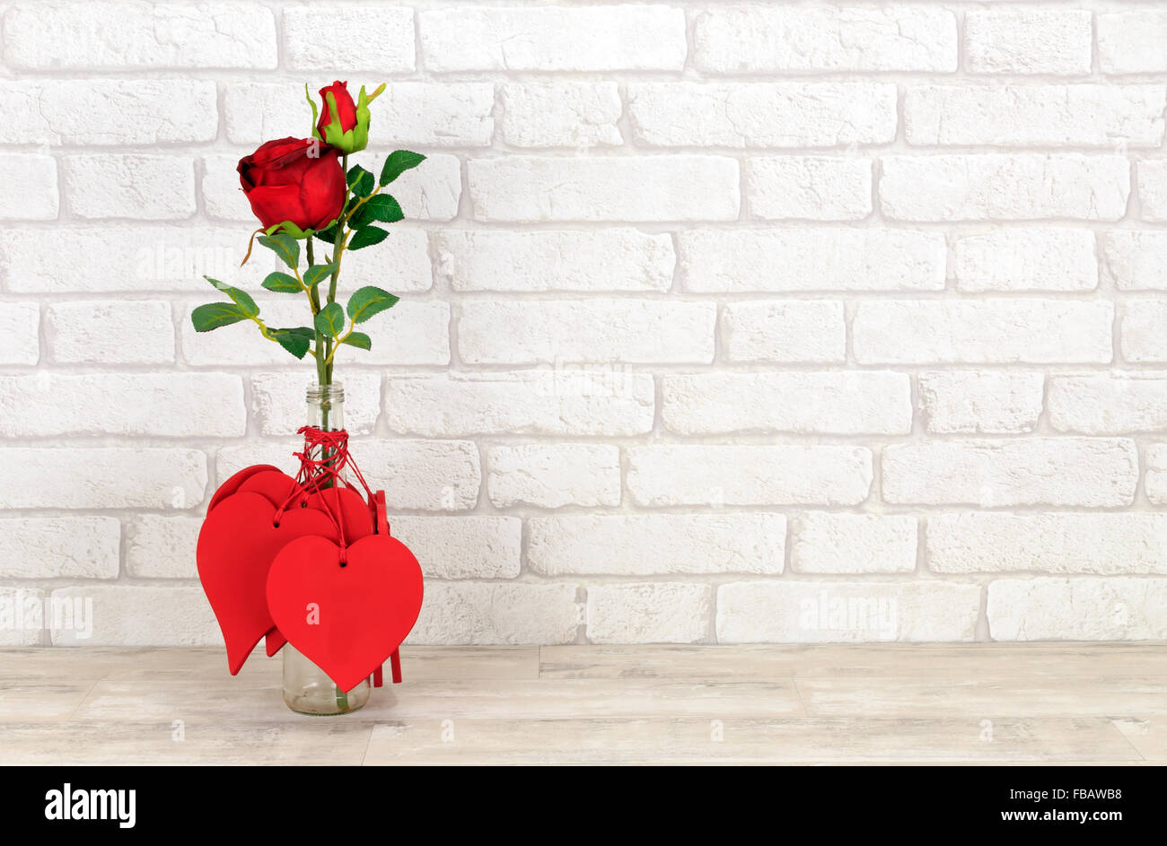 Cuori di San Valentino e rosa rossa in una bottiglia di vetro poste su una squallida scaffale di legno con mattoni bianchi sullo sfondo di parete Foto Stock