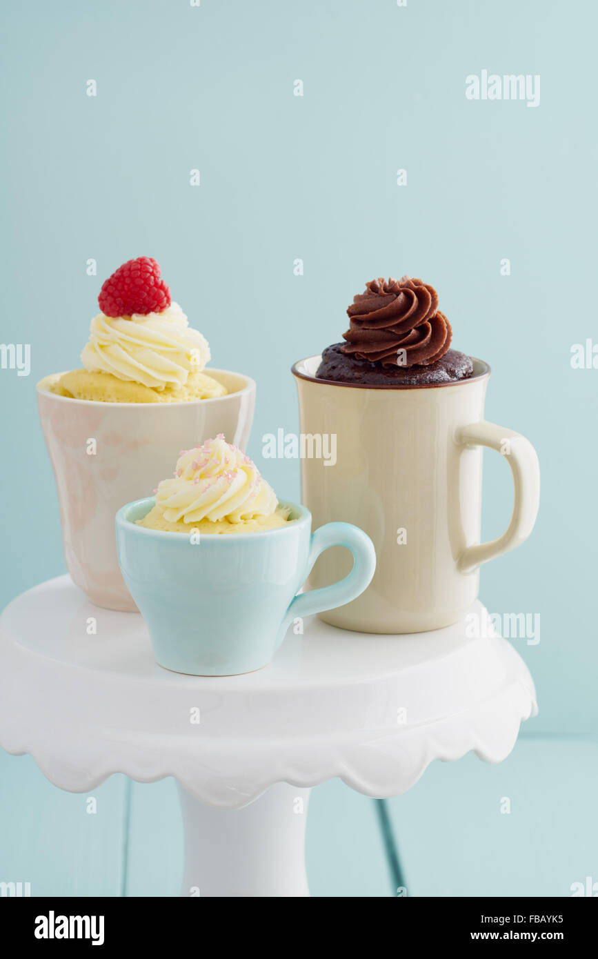 Vaniglia e cioccolato mug di torte con la glassa e lamponi su una torta di stand Foto Stock