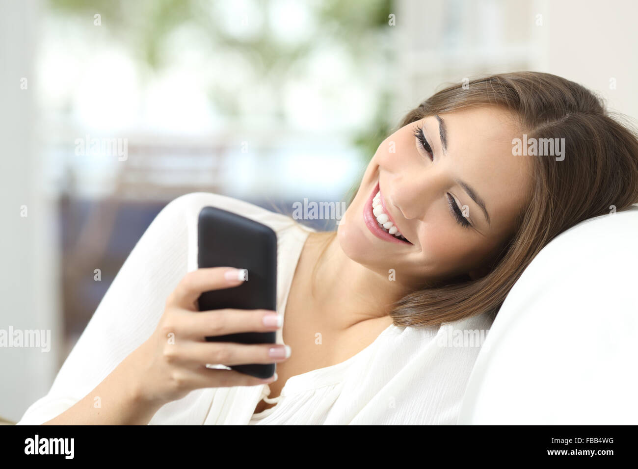 Felice ragazza scrivere messaggi su un telefono cellulare in appoggio su un lettino a casa Foto Stock