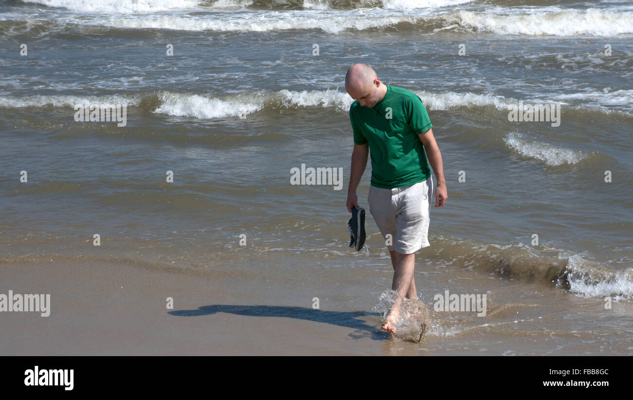 Giovane uomo caucasico schizza acqua su i suoi piedi sulla spiaggia di Da Nang, Vietnam. Foto Stock