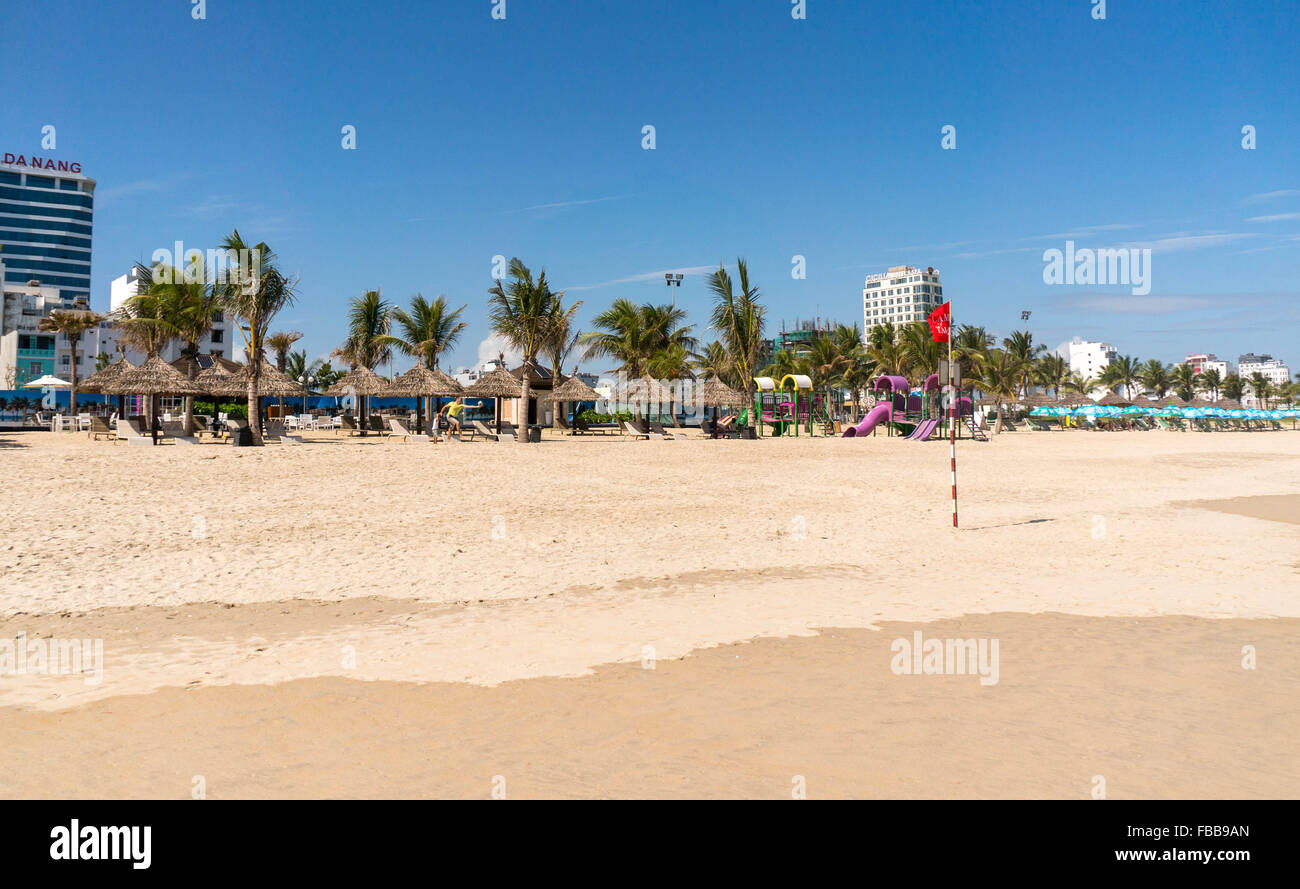 Le palme sulla spiaggia di Da Nang, Vietnam. Una bandiera rossa è volare. Alberghi e un parco giochi per bambini in background. Foto Stock