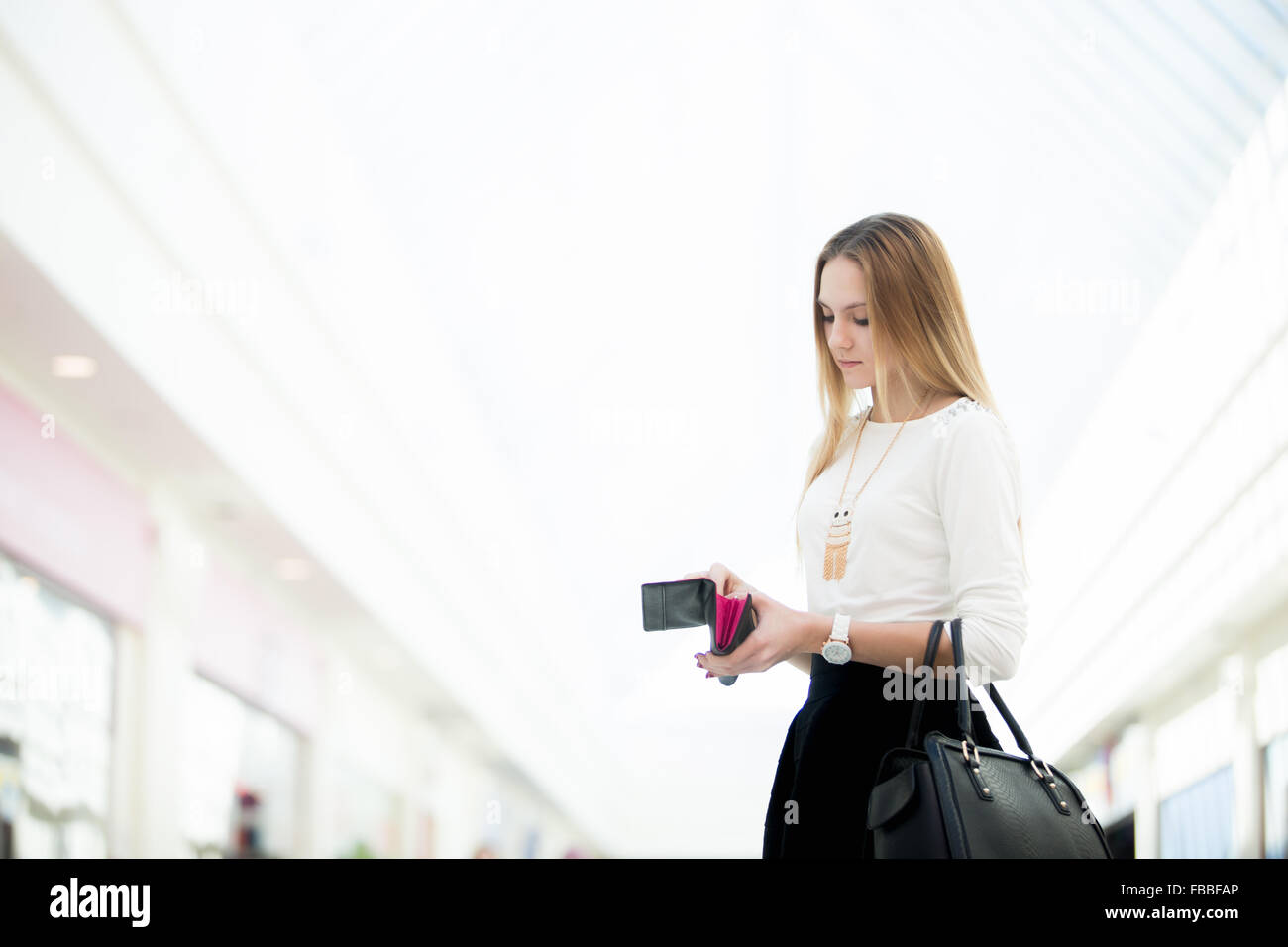 Giovane bella donna in abiti eleganti con borsetta in pelle controllando il suo portafoglio nel centro commerciale. Copyspace Foto Stock