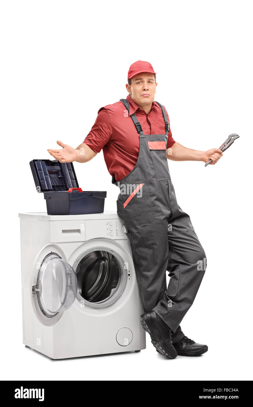 A piena lunghezza Ritratto di un incerto plumber in piedi accanto ad una macchina di lavaggio e di gesti con le mani Foto Stock