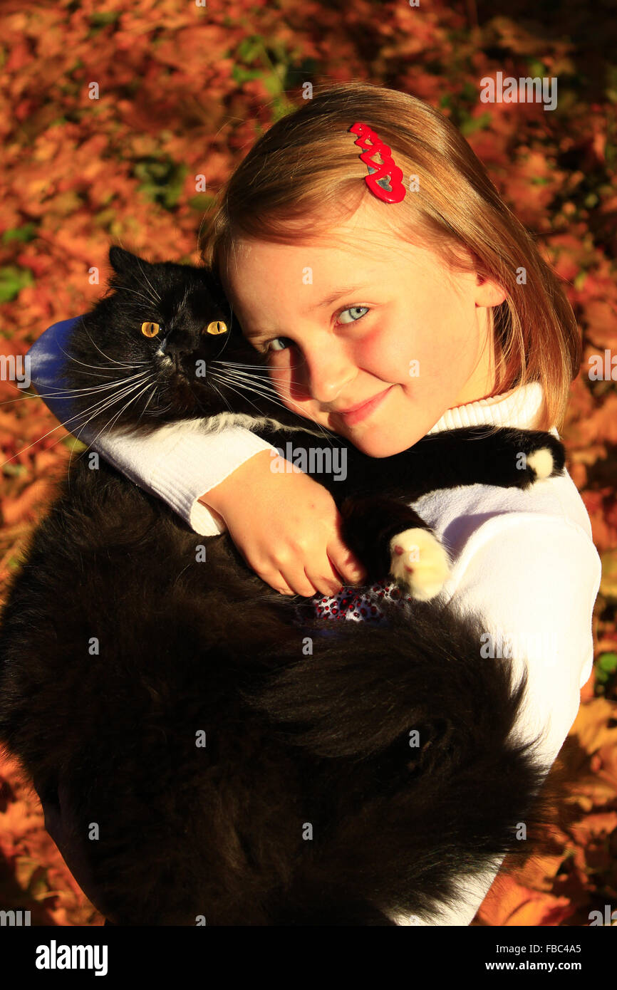 Bambina abbracciare con il suo gatto nero in autunno Foto Stock