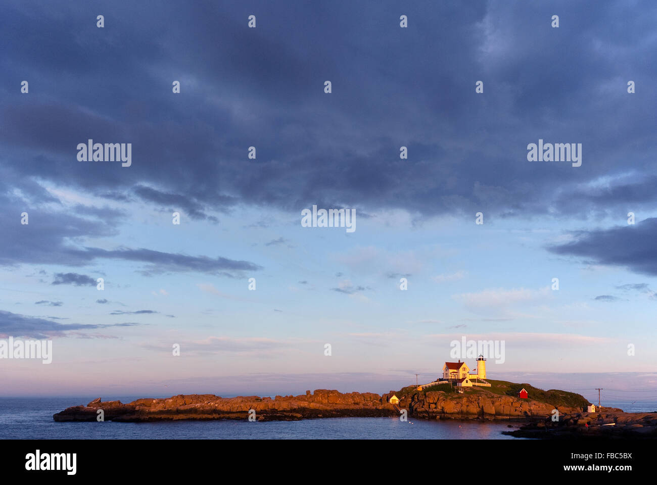 Sun set nella parte anteriore del Nubble (Capo Nededick) faro come nuvole temporalesche approccio su una serata estiva nel Maine. Foto Stock