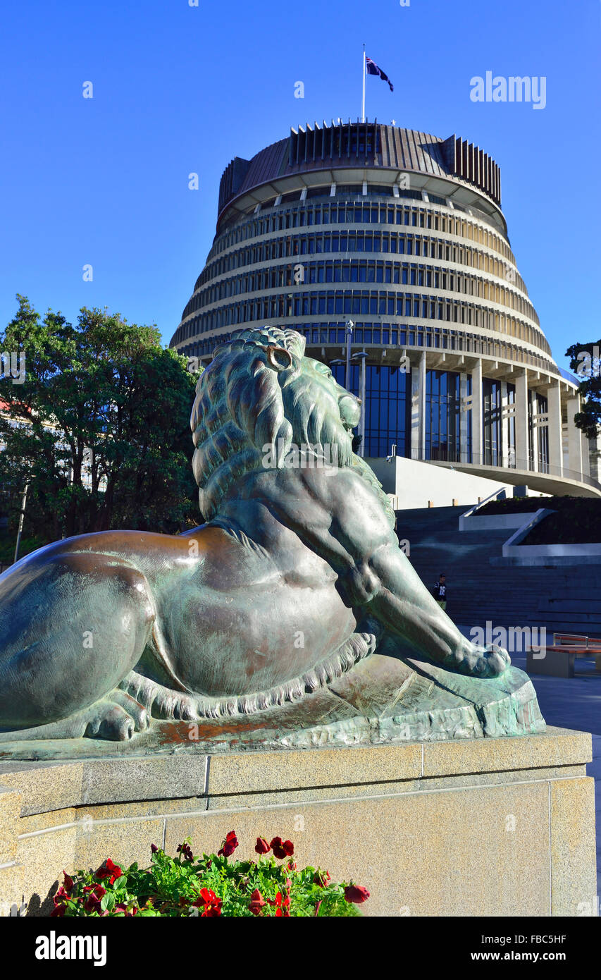 Uno dei due leoni di bronzo sul cenotafio di Wellington con il Parlamento (il Beehive) alle spalle, il Parlamento Grounds, Wellington, Nuova Zelanda Foto Stock