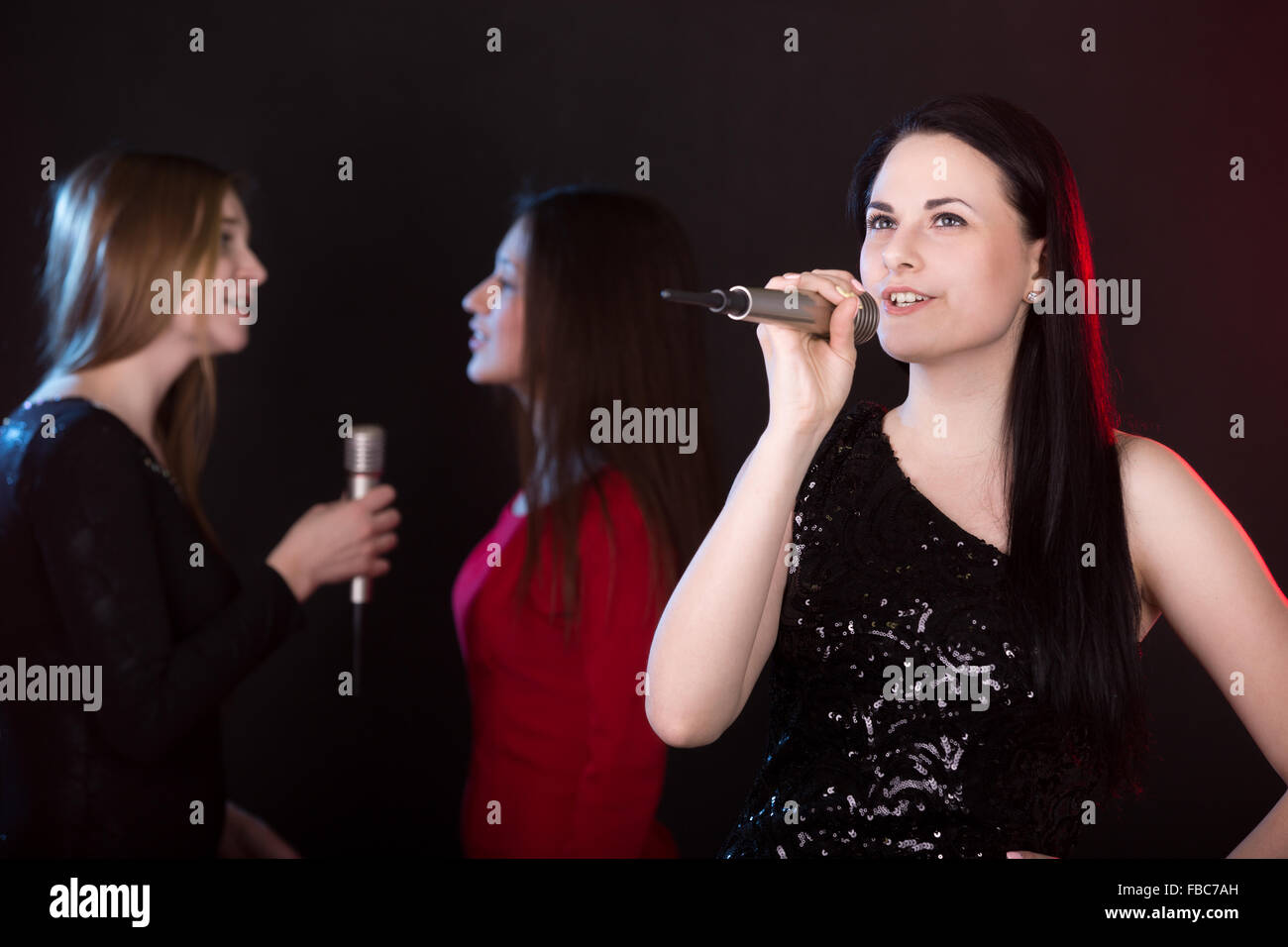 Ritratto di ragazza bella cantante con microfono cantando lyric love song, indietro cantanti sullo sfondo Foto Stock