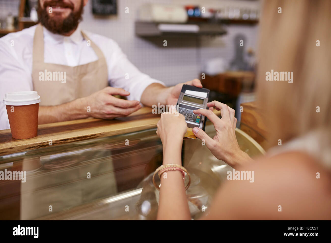 Giovane donna di pagare per un caffè con carta di credito presso la caffetteria. Focus sulla donna mani immettendo il PIN di sicurezza in un lettore di carte di credito. Foto Stock