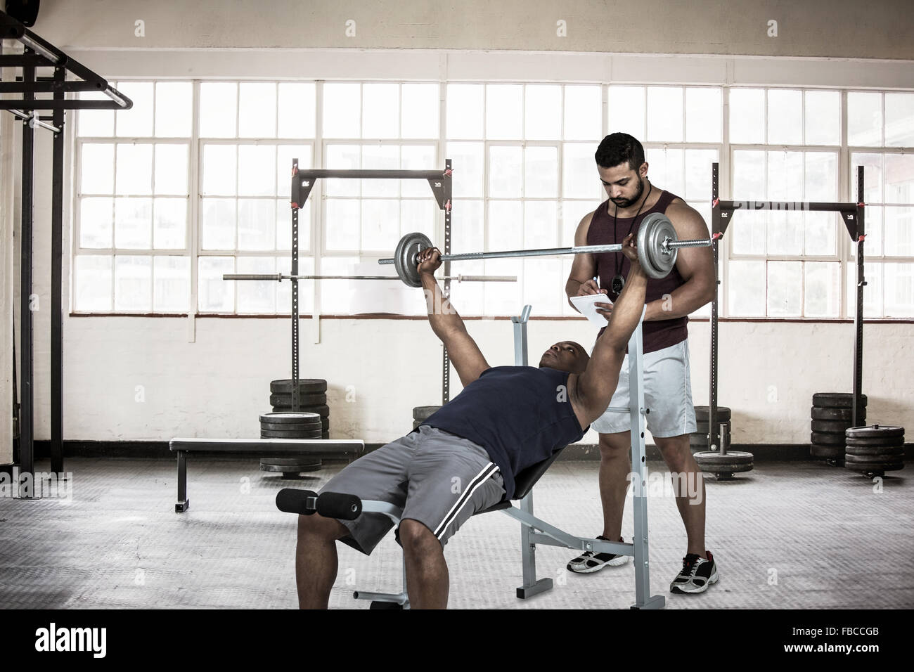 Immagine composita del trainer muscolare aiuta l uomo a sollevare il barbell Foto Stock