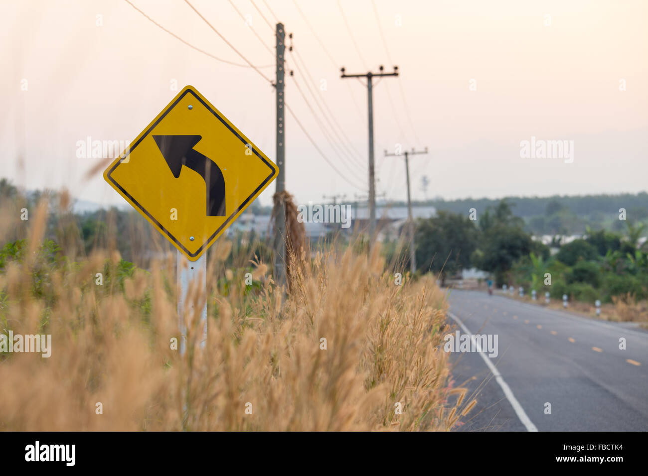 Traffico giallo segno accanto alla strada asfaltata nelle zone rurali della Thailandia nel tramonto Foto Stock