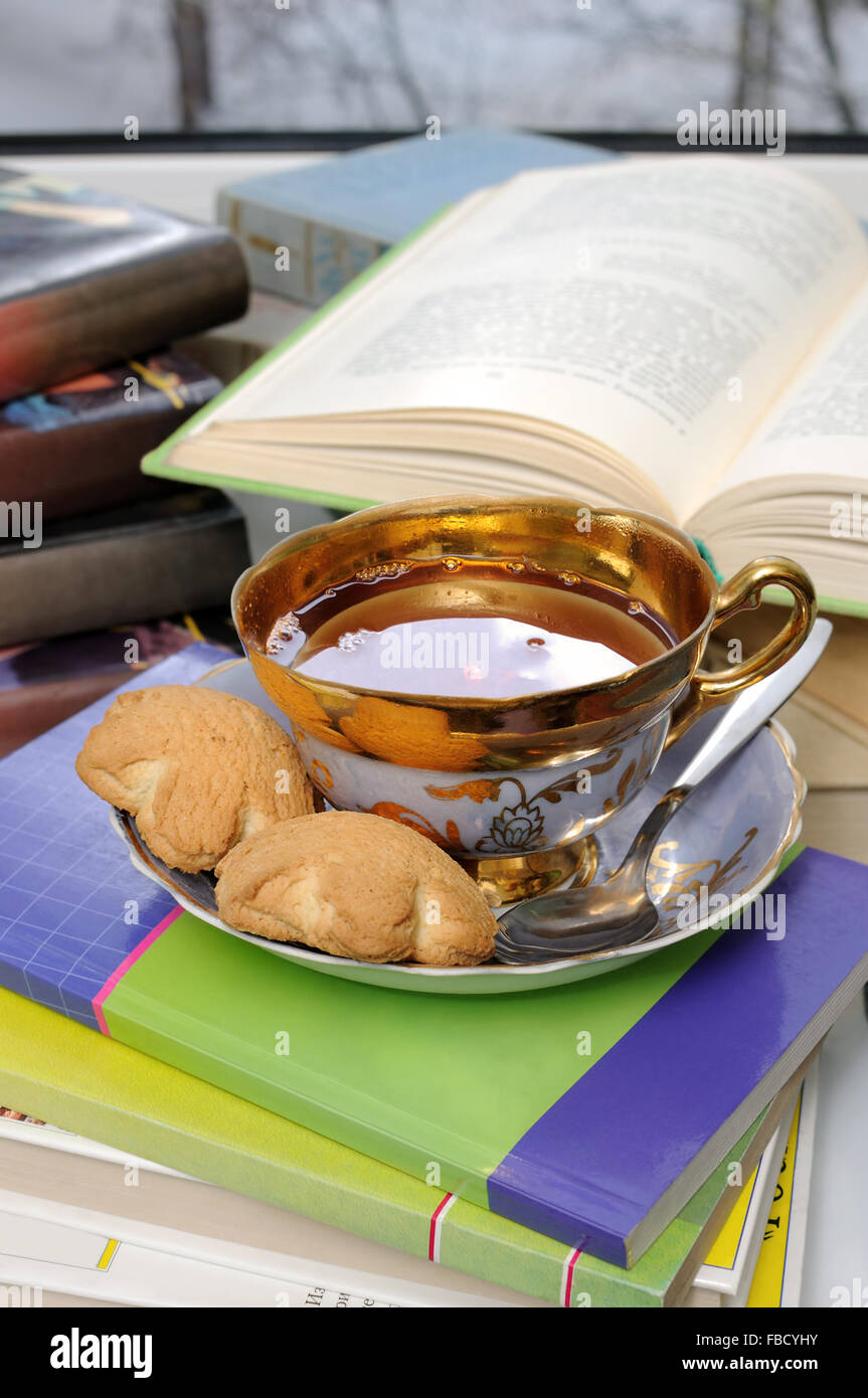 Una tazza di tè e biscotti sul tavolo con libri Foto Stock