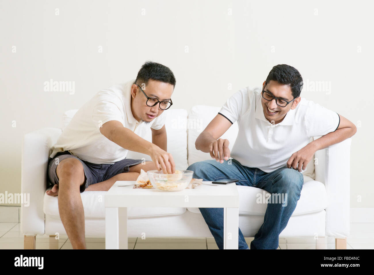 Gli uomini parlare del concetto. Due giovani amico maschio raccolta, chiacchierare e mangiare a casa. Multirazziale persone amicizia. Foto Stock