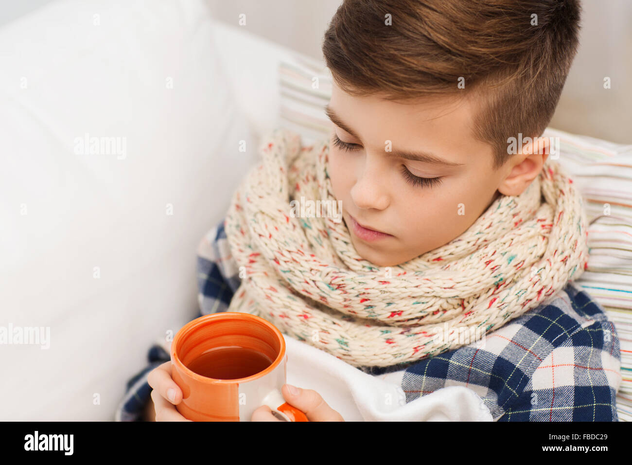 Ragazzo malato con flu in sciarpa bere il tè a casa Foto Stock