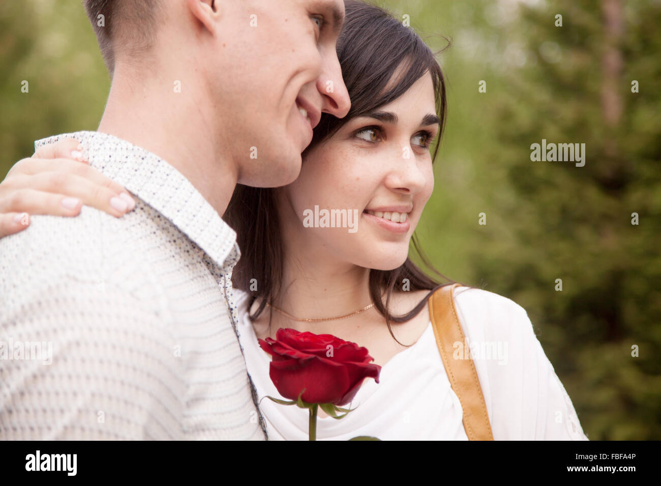 Coppia di amanti dating in park, sorridente giovane donna azienda red rose, abbracciando il suo fidanzato Foto Stock