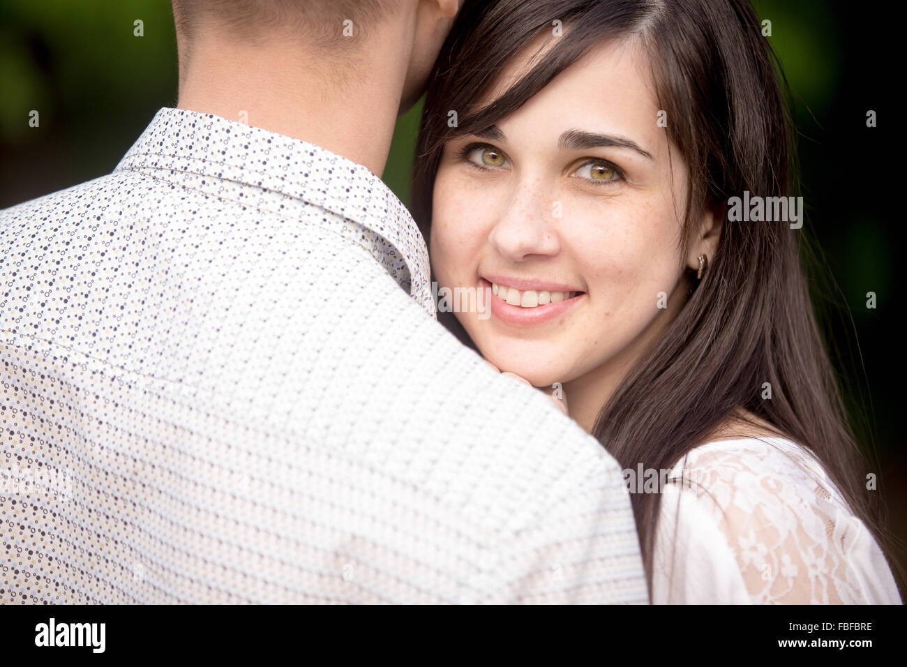 Ritratto di giovane bella bruna sorridenti donna cuddling con il suo fidanzato, nascondersi dietro la sua spalla Foto Stock